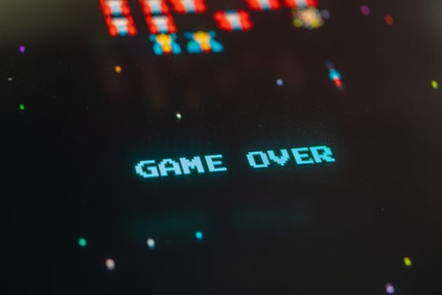 Vintage arcade screen displays GAME OVER in a classic font with a pixelated background, featuring shades of green, yellow, and red Additional colorful shapes and lines add to the nostalgic feel agai