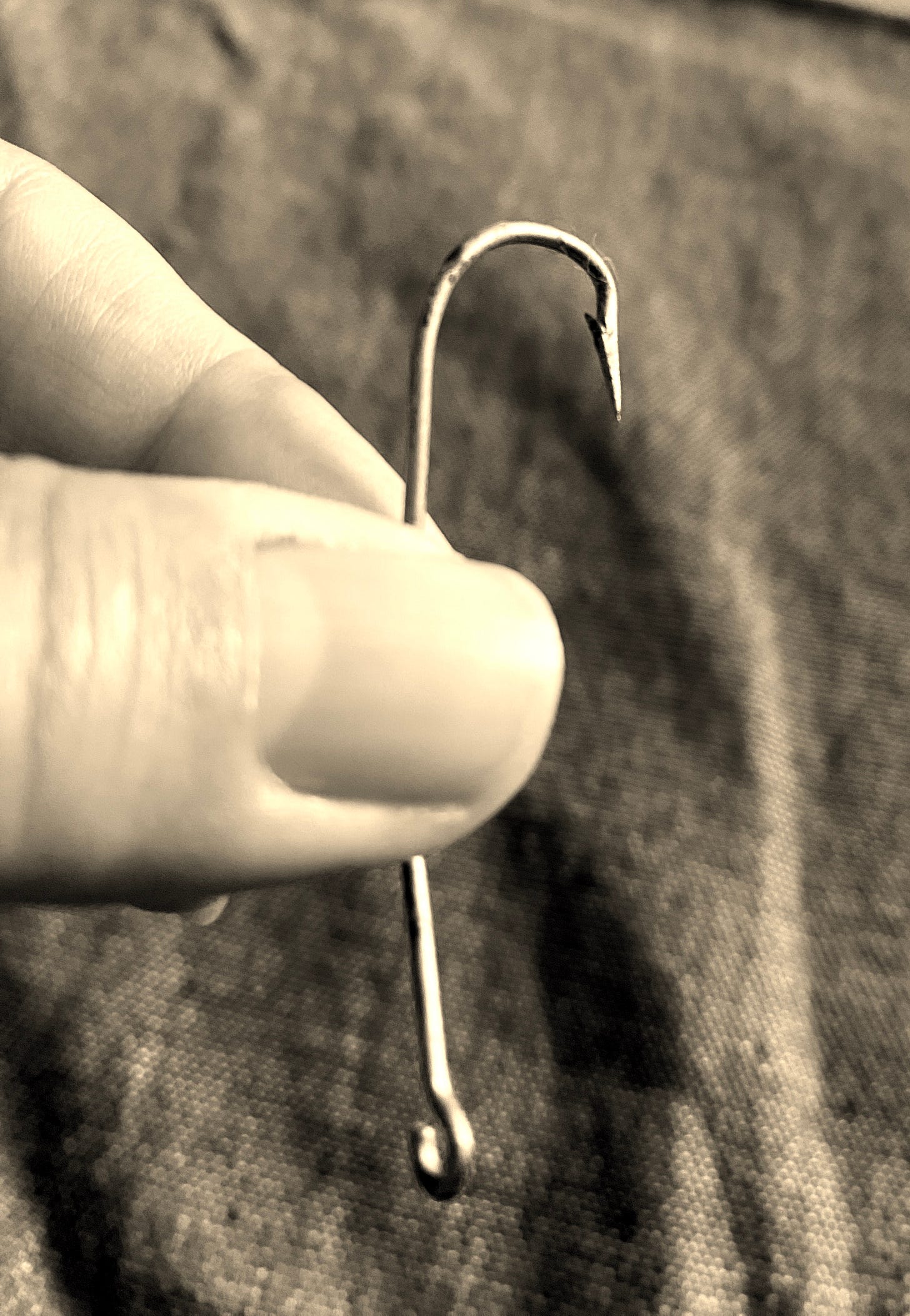 3 inch fish hook held between thumb and index finger