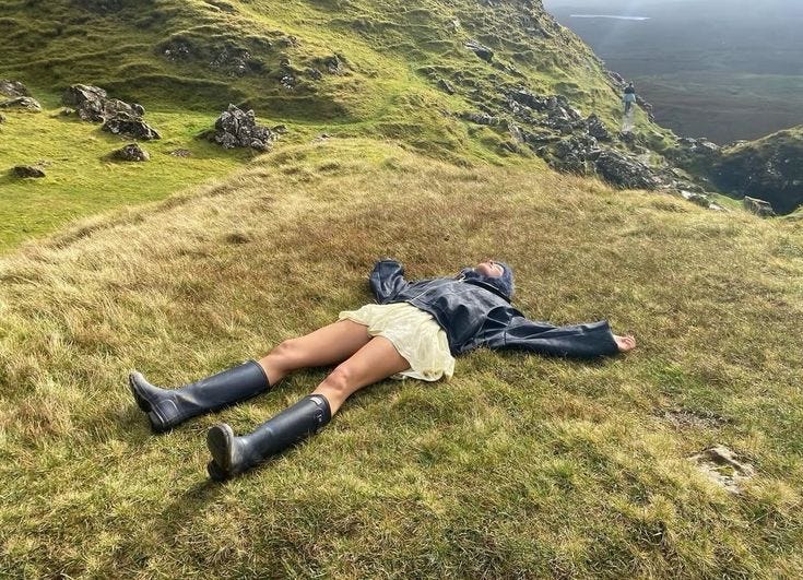 This may contain: a woman laying on top of a lush green hillside