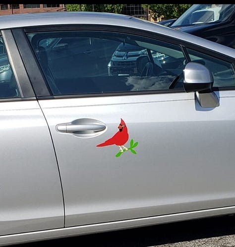 A cardinal mosaic in a shop with "please ask for assistance" under it, a cardinal in a tree sculpture in a park, and a cardinal stencil on a silver car door in a parking lot.