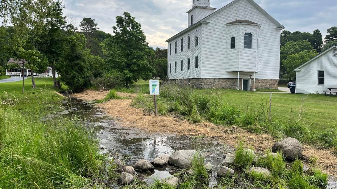 The image depicts a small, white church building with a weather vane on top, surrounded by a grassy area, a small stream, and some scattered rocks.
AI-generated content may be incorrect. The image depicts a small, white church building with a weather vane on top, surrounded by a grassy area, a small stream, and some scattered rocks.
AI-generated content may be incorrect.