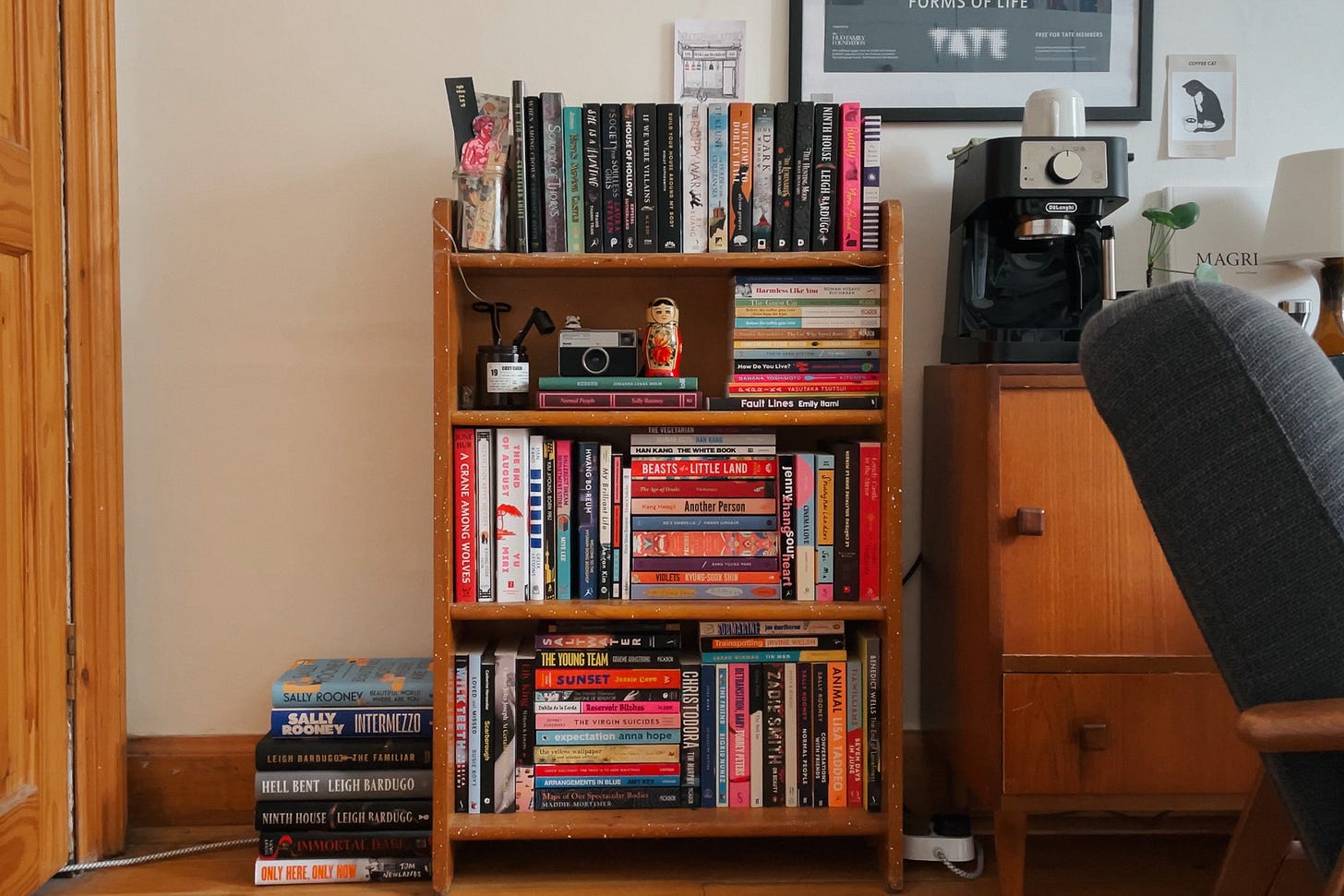 A wide shot of a neatly organised bookshelf in a cosy flat, surrounded by furniture and home decor