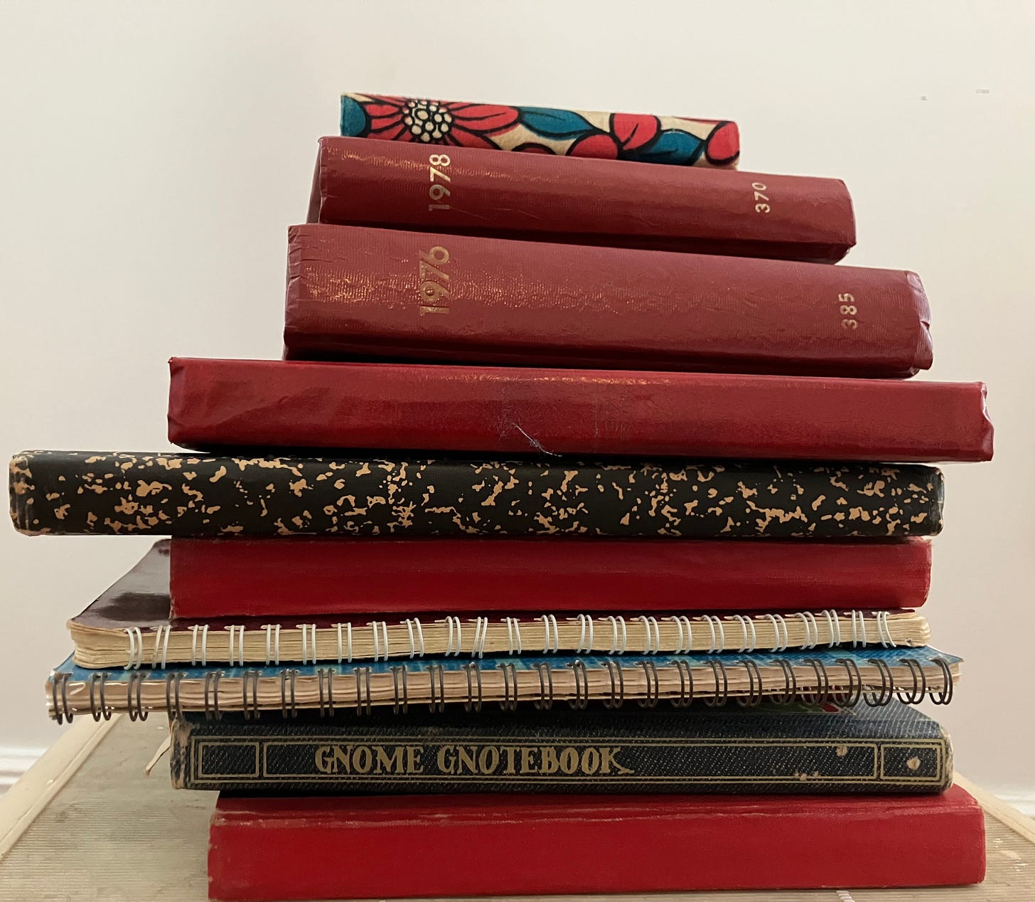 stack of ten bound books, mostly red with embossed gold dates, a few wirebound notebooks.