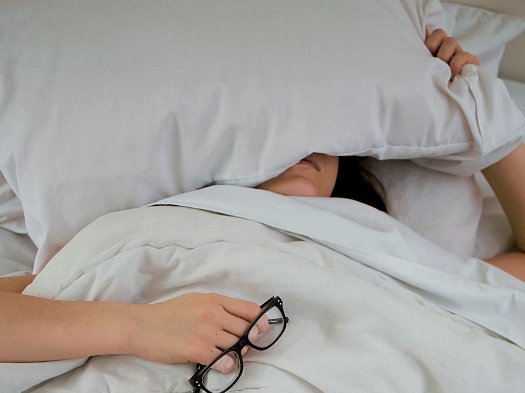 person lying on bed while covering face with pillow and holding eyeglasses person lying on bed while covering face with pillow and holding eyeglasses