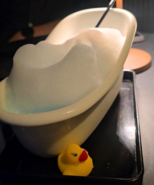 A cocktail in a bath tub with a rubber duck next to it