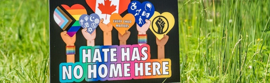 Yard sign saying he has no home here. Different colored arms are holding hearts showing pride/interreligious symbols, accessibility symbols, black pride symbol, Canadian flag. Yard sign saying he has no home here. Different colored arms are holding hearts showing pride/interreligious symbols, accessibility symbols, black pride symbol, Canadian flag.