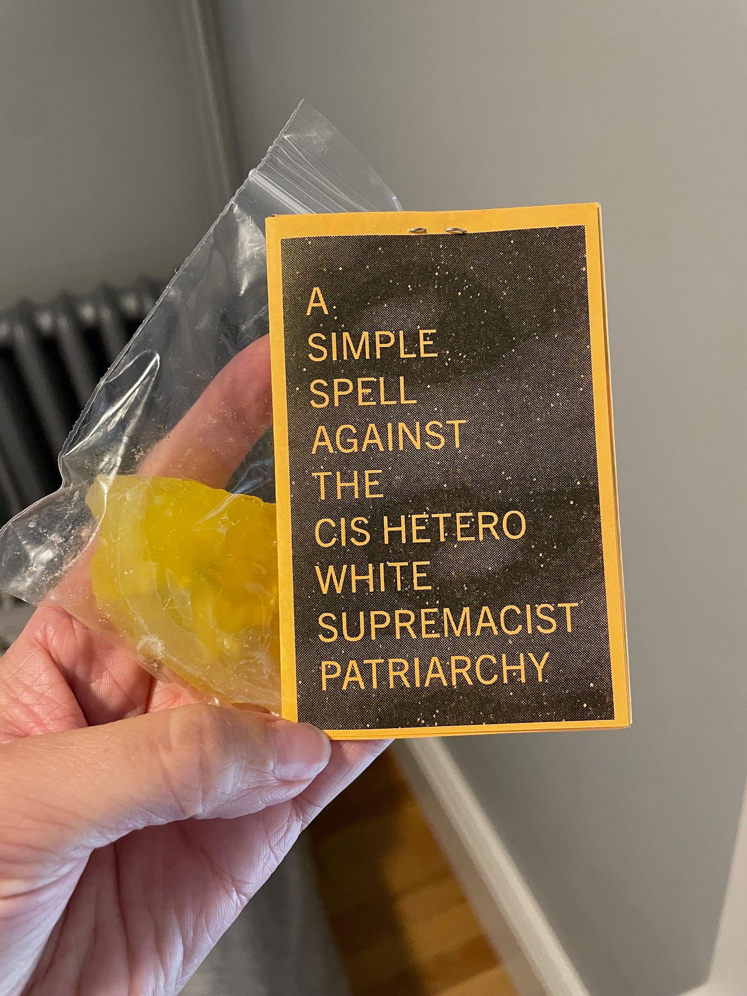 Photo of a white woman's hand holding a folded zine with a photocopied image of what looks like a planet with the words: A simple spell against the cis hetero white supremacist patriarchy