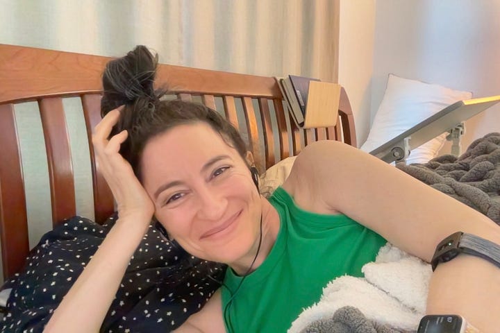 On the left, a girl with brown hair and watery eyes looks pained or concerned. She wears a black top, black wired headphones, and lays on a bright blue pillowcase. On the right, the same girl is smiling, lying sideways on her bed, wearing a bun and a green tank top in front of a brown slatted headboard.