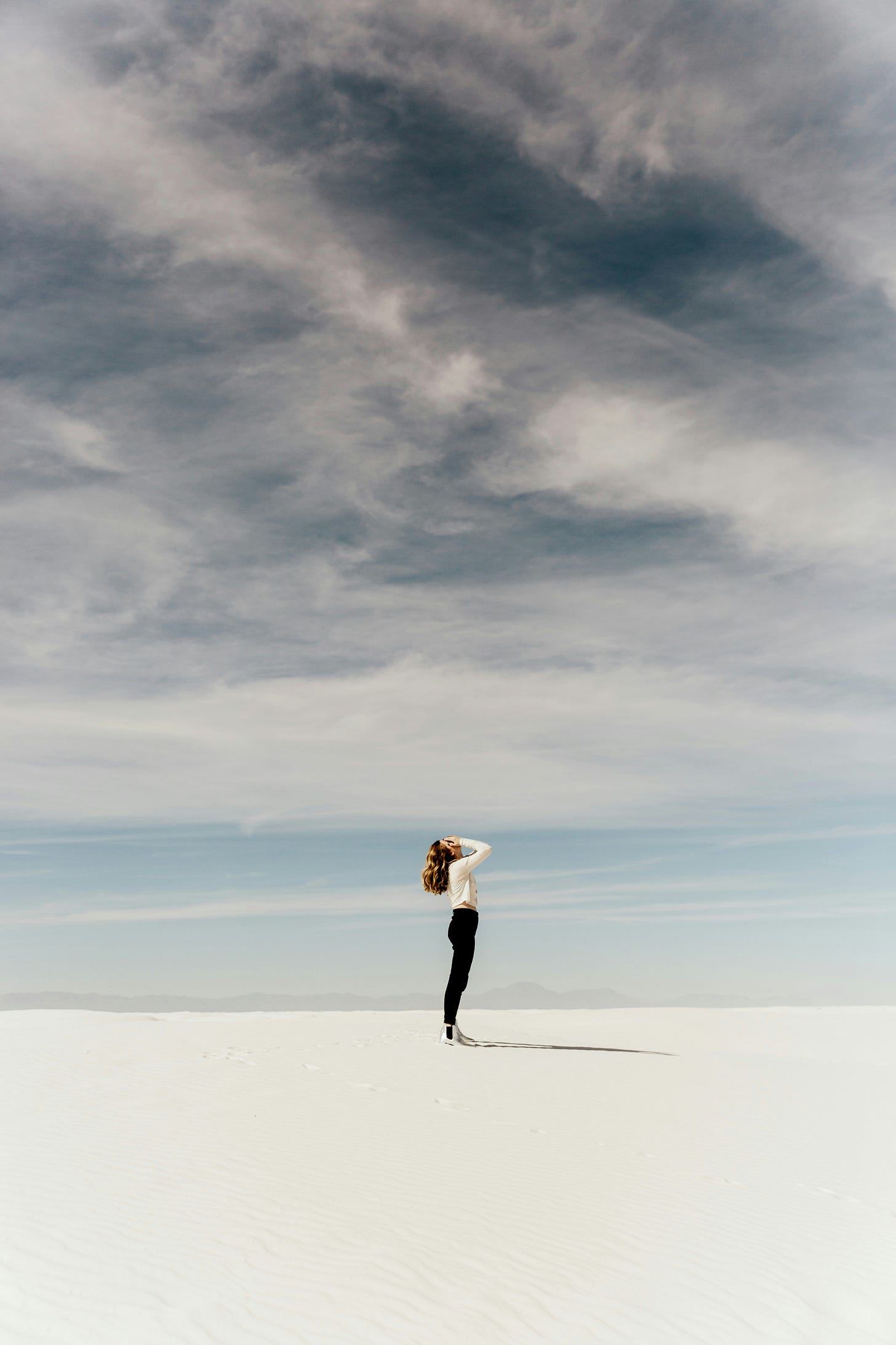 woman looking at the sky and holding her head while standing on white sand