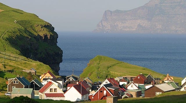 This may contain: a group of houses sitting on top of a lush green hillside next to the ocean