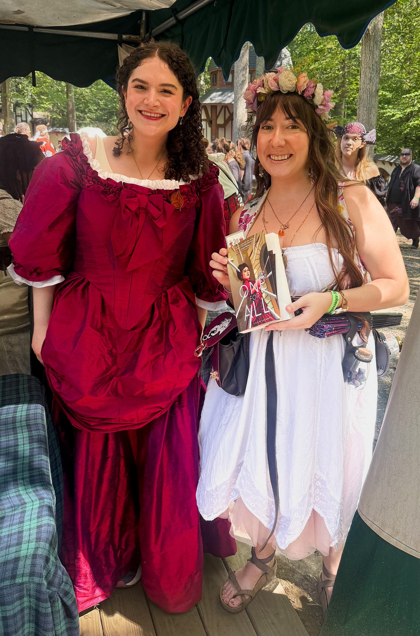 Kaite and Lilli Lainoff at the Maryland Renaissance Festival with Kaite holding Lilli's novel One for All. 