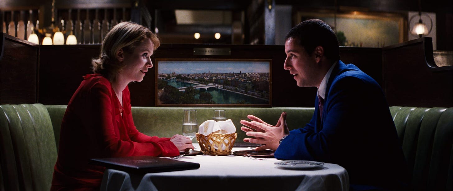 Punch-Drunk Love | Still features Adam Sandler in a blue suit sitting across a table from a red-clad woman named Lena Leonard played by Emily Watson.