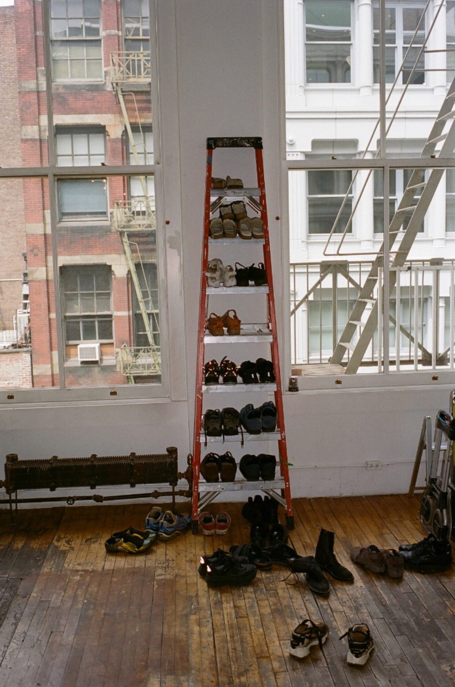 SoHo loft window wall with a ladder used as vertical shoe storage; pairs lined up on wood floors