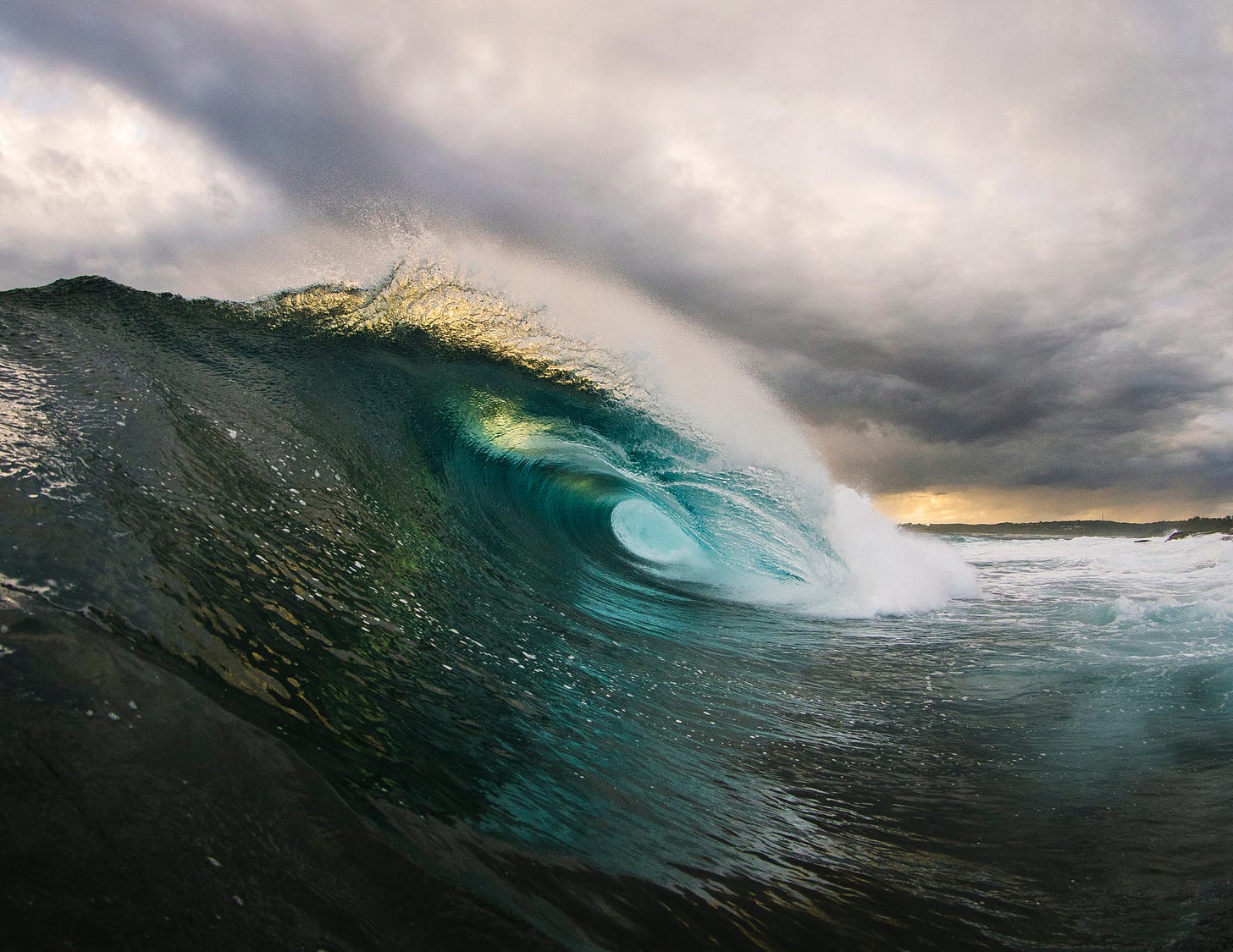 A huge wave in the ocean, with clouds above in the sky.