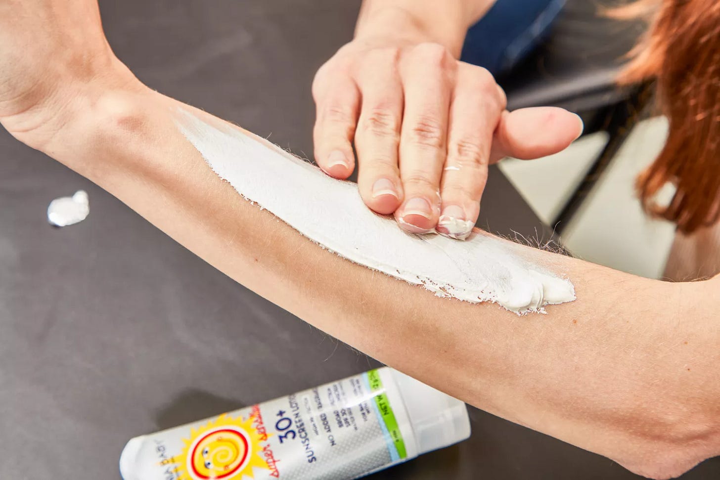 Person's hand smears California Baby Super Sensitive SPF 30 Lotion across an arm