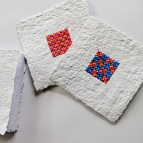 Handmade paper notebook bound using Japanese stab binding method with blue cross stitched square centre.