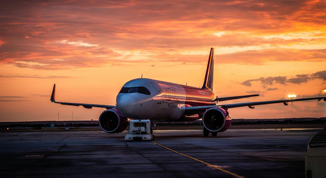 A plane on a runway with a sunset sky above it