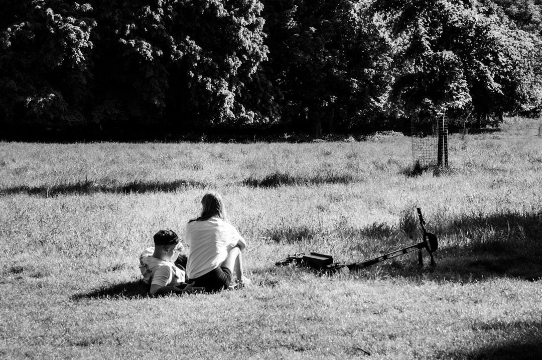 Two people sitting on grass in a park.