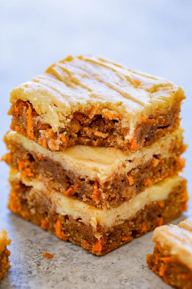 A stack of three cream cheese carrot cake bars, the top bar missing a bite. 