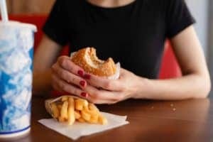 Young girl holding in female hands fast food burger, american unhealthy meal on blue background, mockup with copy space for text message or design, hungry human with grilled hamburger front view