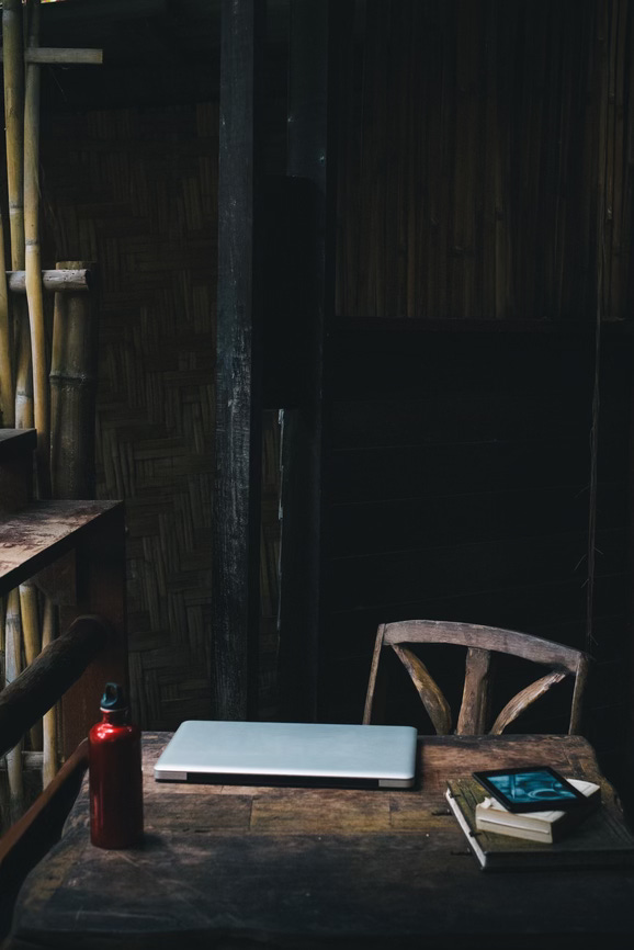 a dark photo of a laptop on a wooden desk in a dark corner