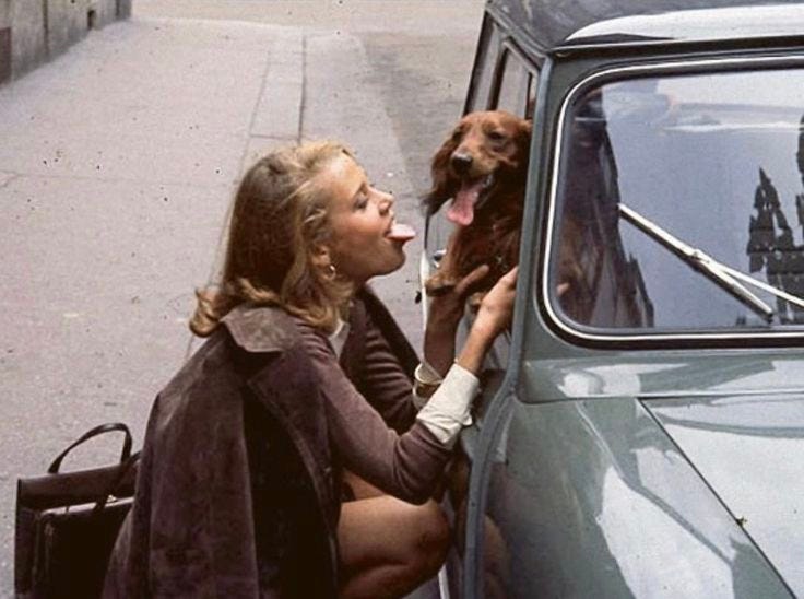 This may contain: a woman sitting on the side of a car with her dog looking out the window