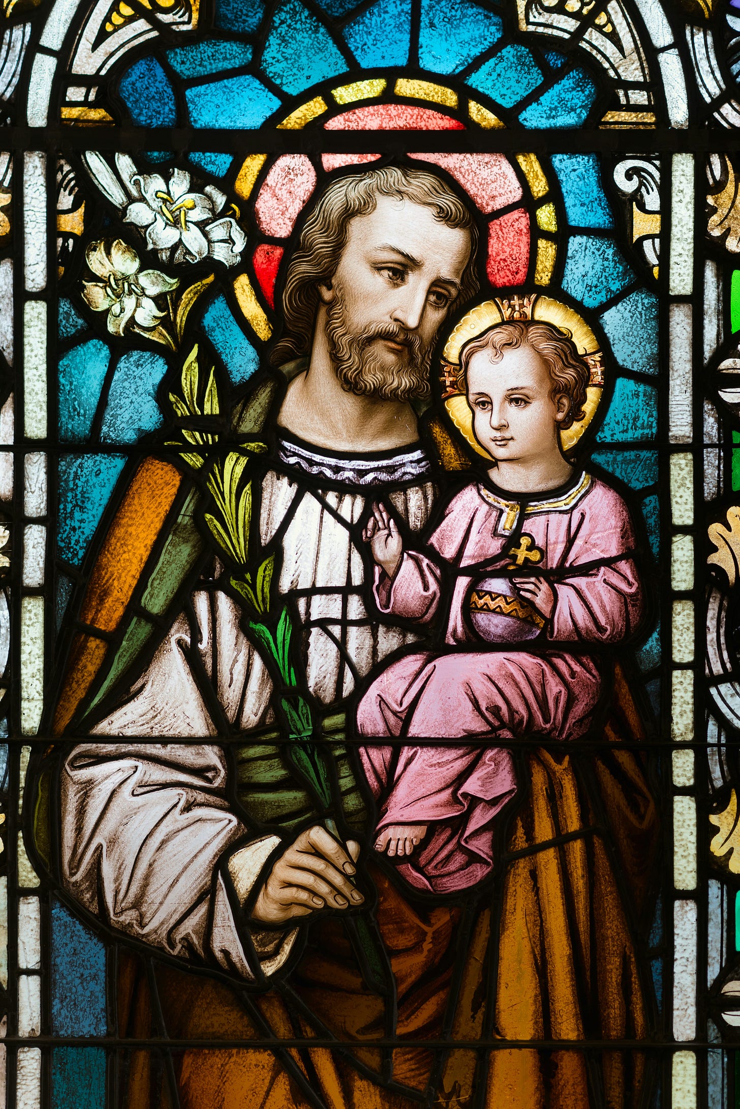 stained glass window of Joseph carrying young Jesus, with halos around their heads and lilies