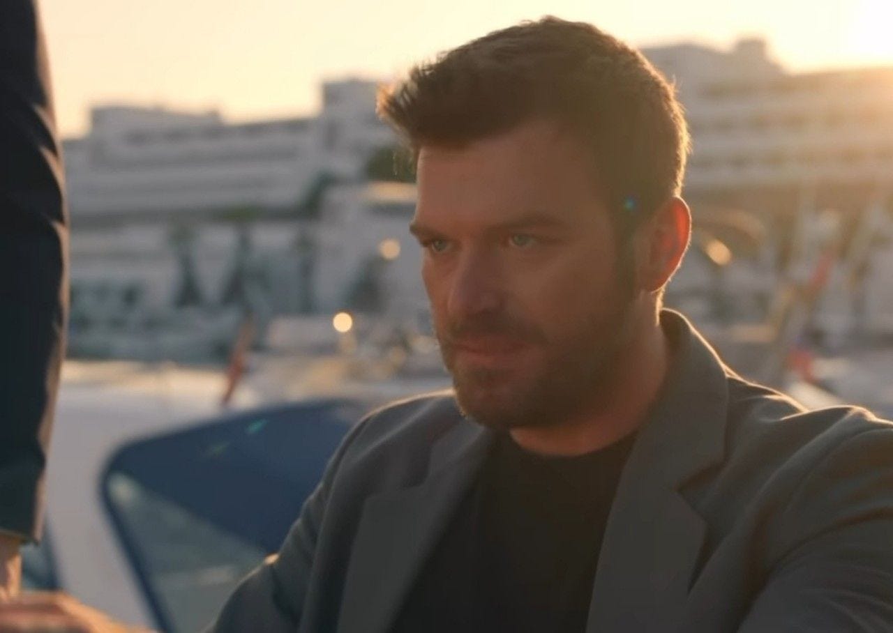 Kıvanç Tatlıtuğ, marinada gün batımında ceketle oturuyor.