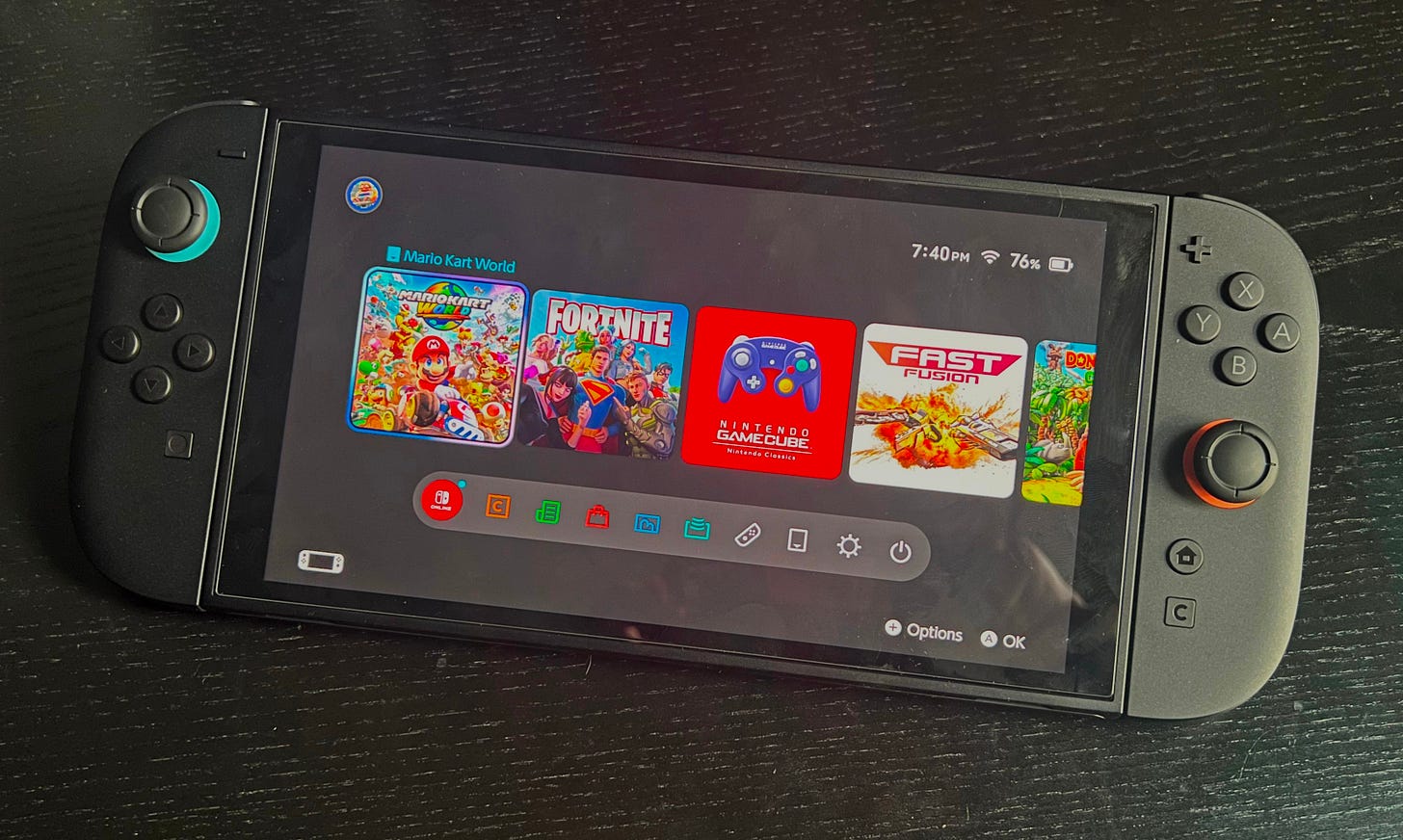 A Nintendo Switch 2 console at the home screen, with four icons visible: Mario Kart World, Fortnite, GameCube classics, and Fast Fusion.