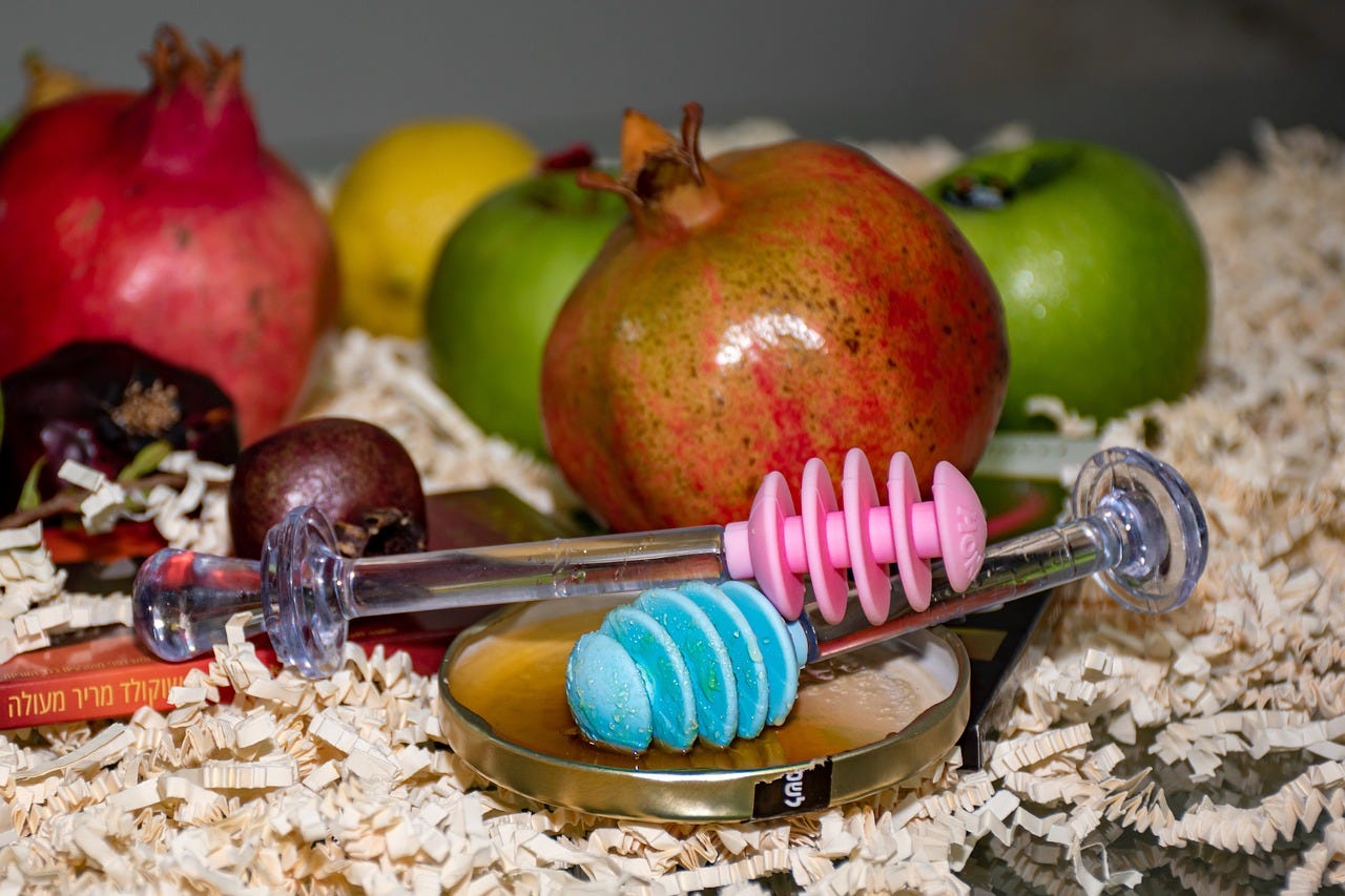 Scene with pomegranates, apples and honey servers laid out on a bed of wood shavings