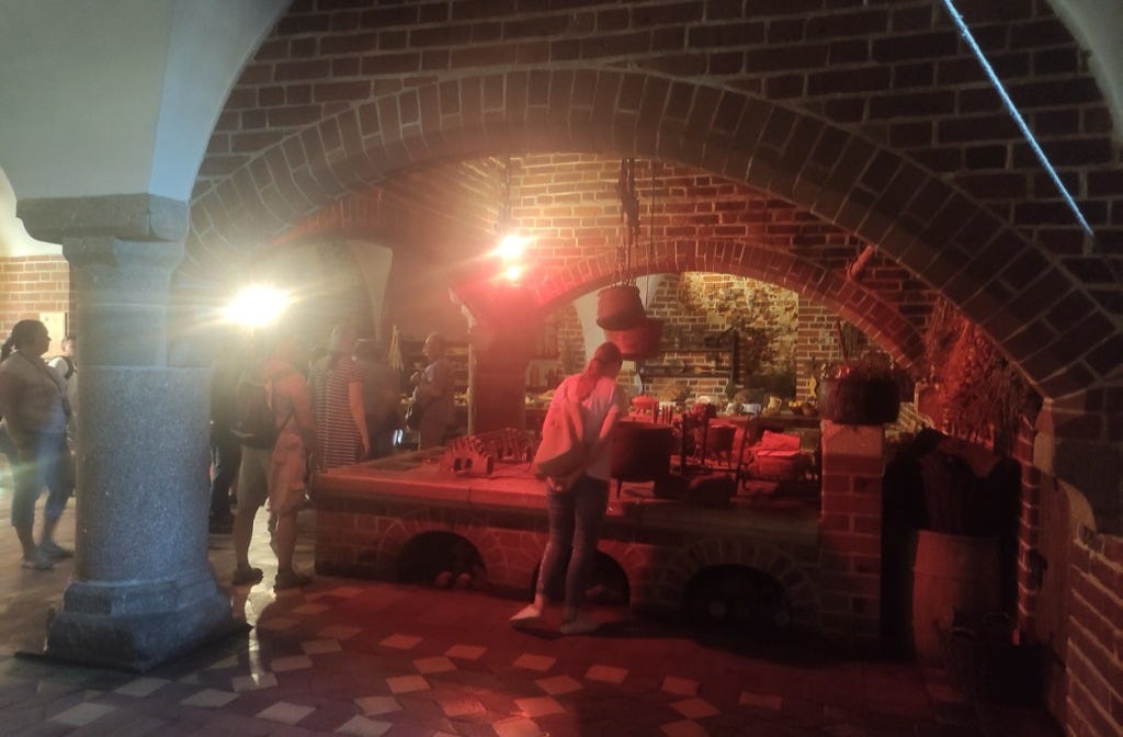 People walk round a huge range in the kitchen, which has arches covering where the fire would have raged. The lighting gives it a red glow.