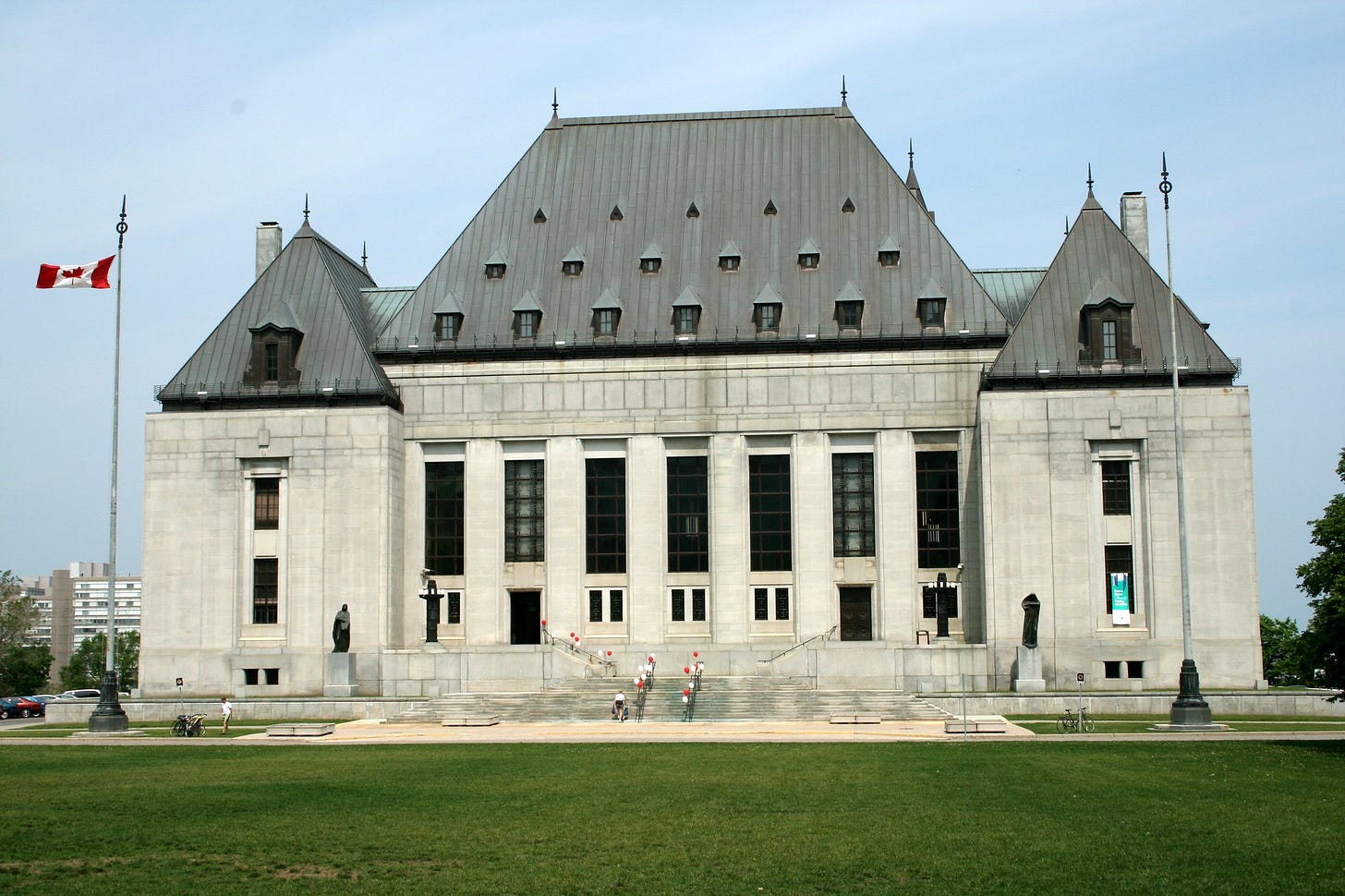 A stock photo of the Supreme Court of Canada building in Ottawa. It's a stone building surrounded by a large grass lawn and with steep greenish roofs. 