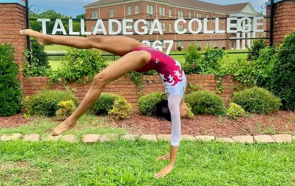 Talladega College gymnastics freshman Jamilia Duffus does a back handspring on the grass in front of a school sign.