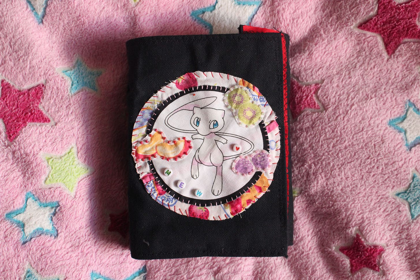a black, clothbound sketchbook with a patch of the pokemon "Mew" sewed to the front of it