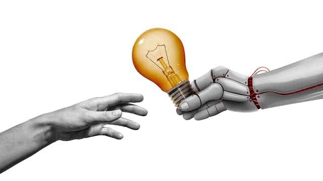 An illustration shows a robotic hand extending a light bulb to a human. An illustration shows a robotic hand extending a light bulb to a human.