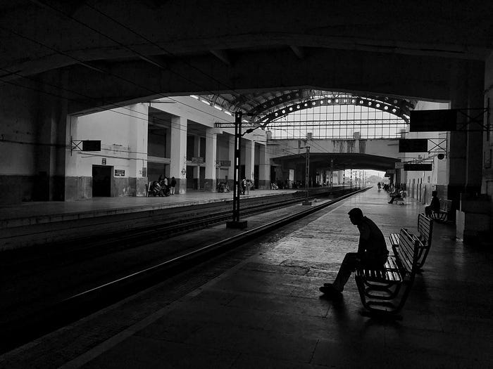 Black and white photo of people sitting on benches, far apart from one another. Isolated and alone. Black and white photo of people sitting on benches, far apart from one another. Isolated and alone.