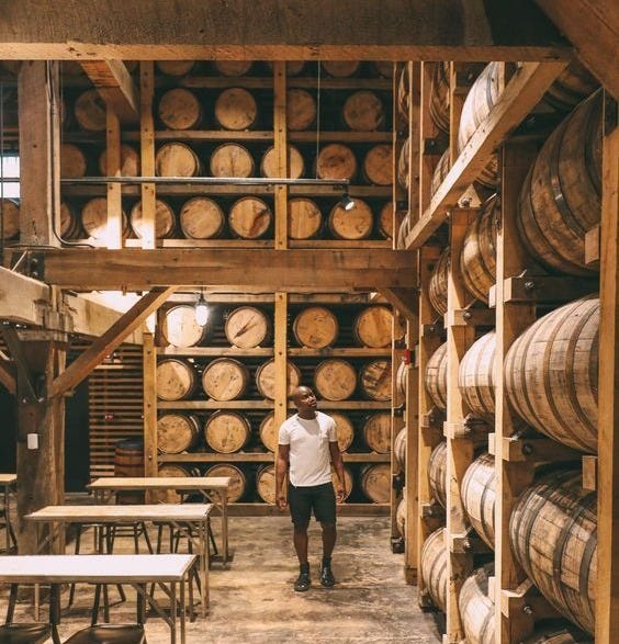 This may contain: a man standing in the middle of a room filled with wooden barrels and tables next to each other