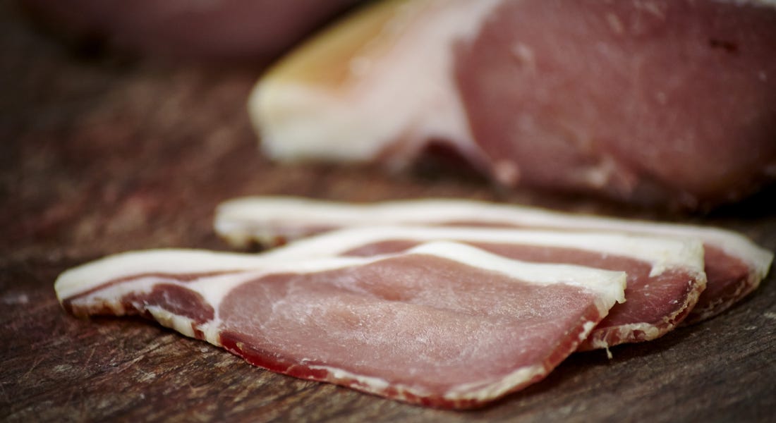 A cut of bacon on a dark wooden board A cut of bacon on a dark wooden board