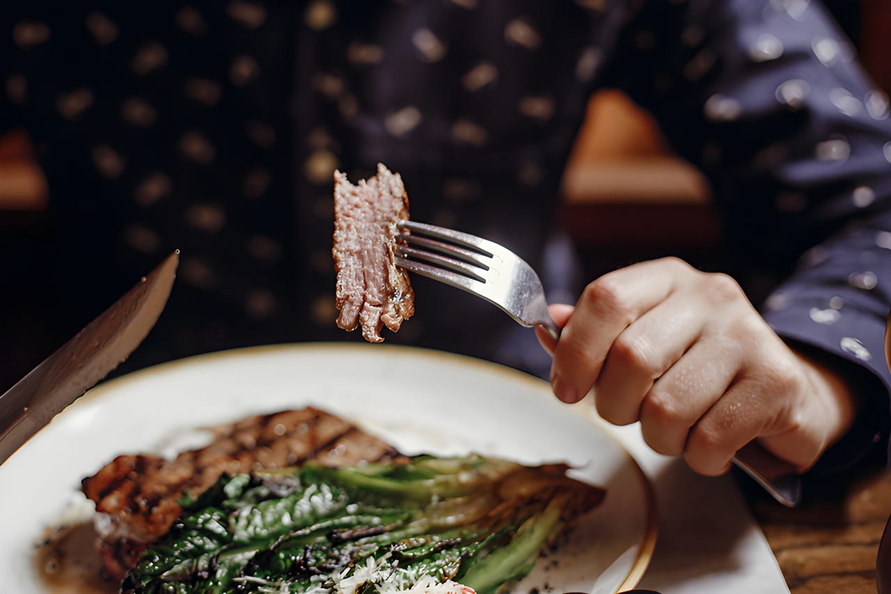Person eating steak with a side of braised greens