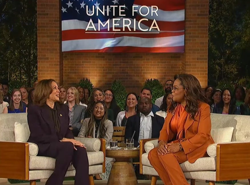 Kamala Harris and Oprah Winfrey, sitting on identical small couches, talk onstage during the online town hall. Video Screenshot.