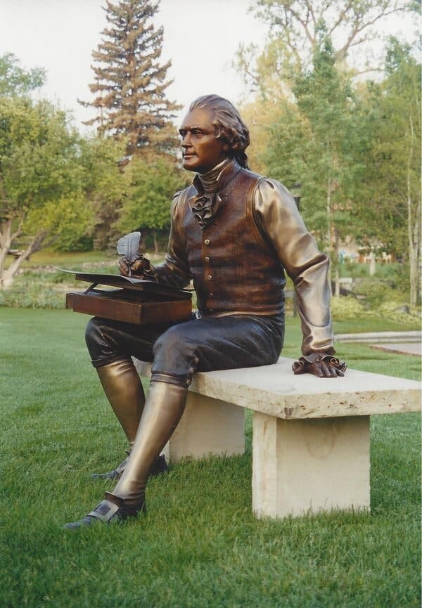 A bronze sculpture of a man seated on a bench. A bronze sculpture of a man seated on a bench.