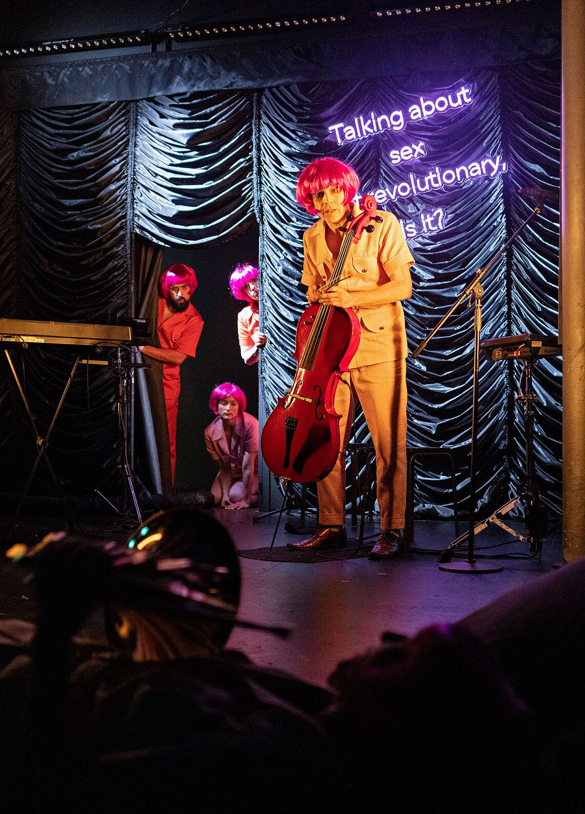 four performers in matching pink wigs look at the audience with curious concern