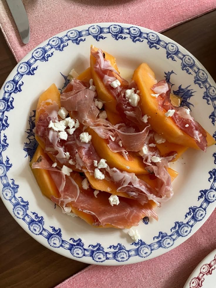 This may contain: a white and blue plate topped with peaches covered in cheese on top of a pink table cloth