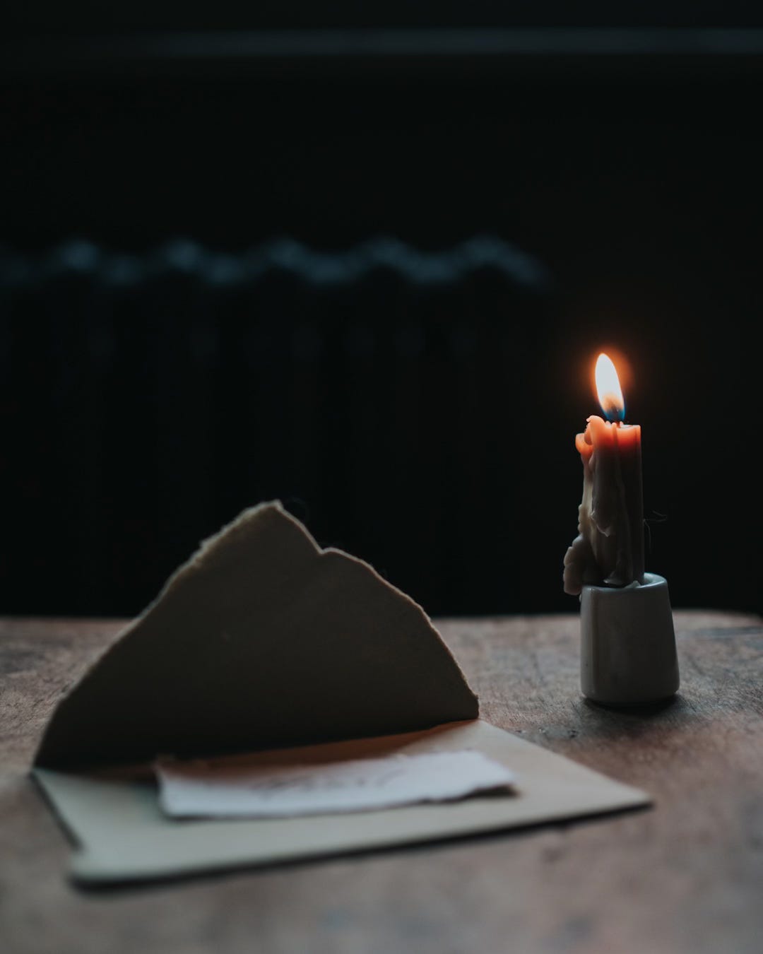 Lit candle and small envelope on a wooden stool