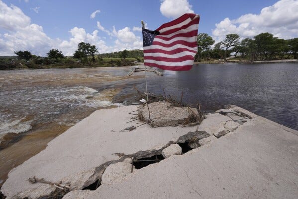 An American flag sits on a destroyed bridge over the Guadalupe River at Arcadia Loop and Bear Creek Road after flooding in Kerrville, Texas on Wednesday , July 9, 2025. (AP Photo/Gerald Herbert)
