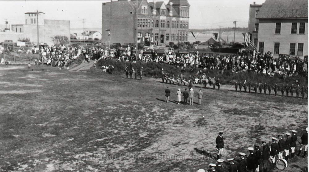 A historic photograph of a parade in Port Townsend with people gathered along a wide street, likely during the Rhododendron Festival.