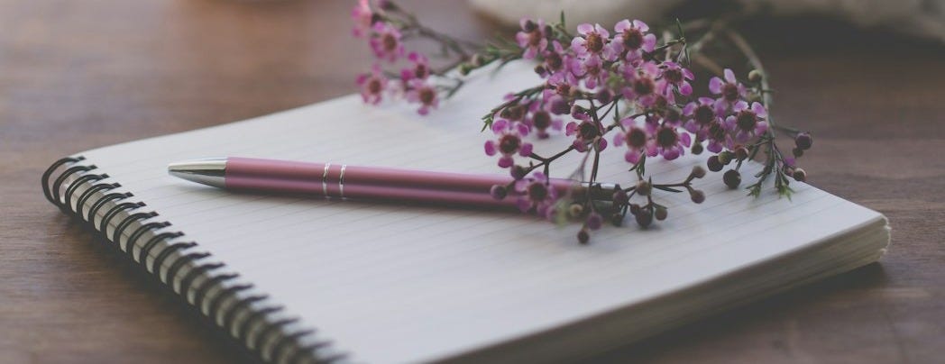 shallow focus photo of purple flowers on white spiral notebook shallow focus photo of purple flowers on white spiral notebook