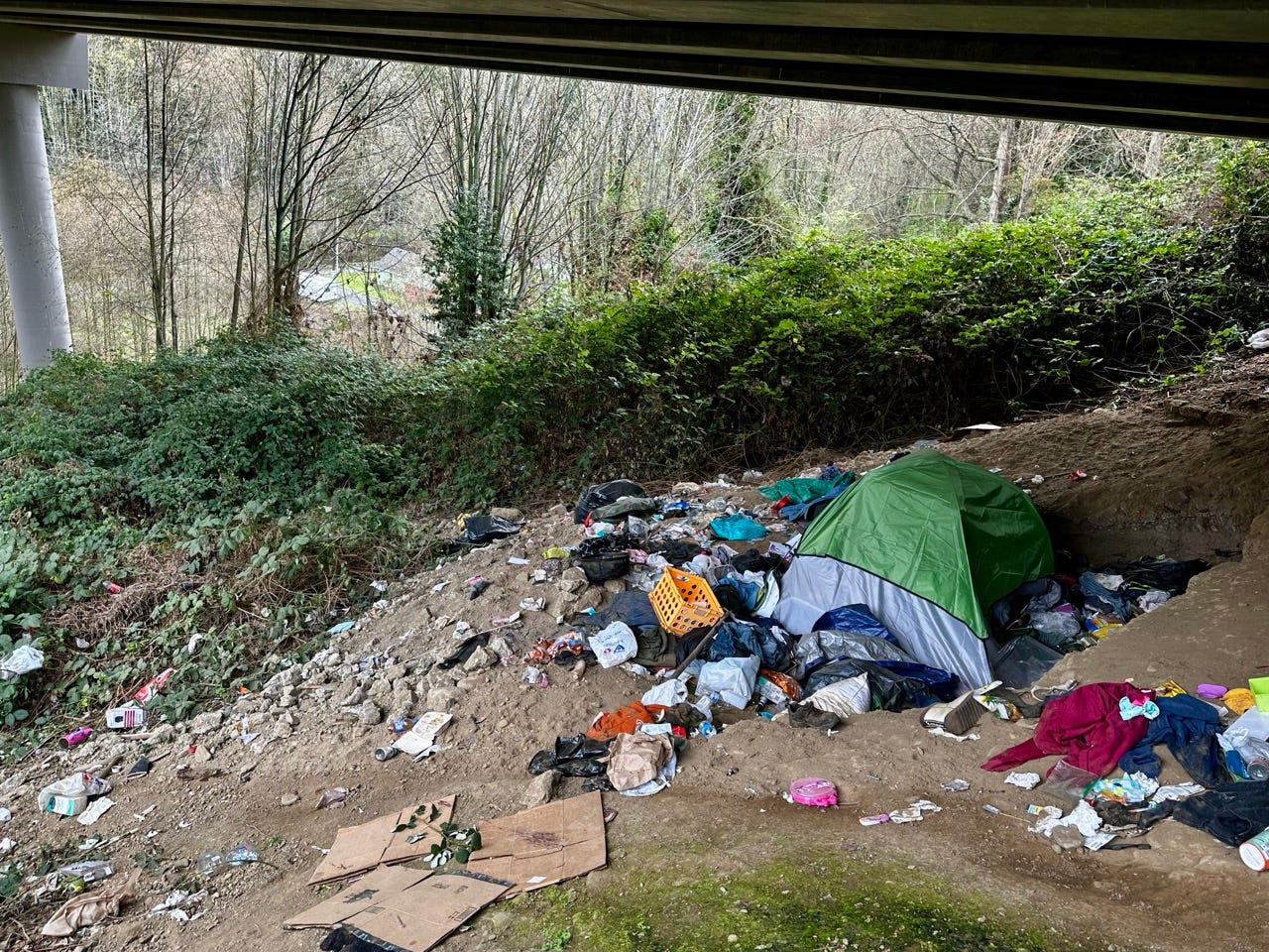A tent in the dirt under a bridge

Description automatically generated