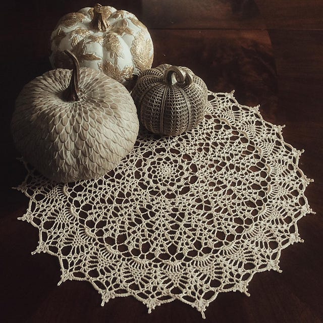 Full view of a beige crochet doily with pumpkins on top, displayed on a wooden surface. Full view of a beige crochet doily with pumpkins on top, displayed on a wooden surface.