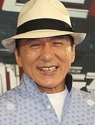 Jackie Chan smiling at the camera while wearing a cream-colored Panama hat with a wide black band Jackie Chan smiling at the camera while wearing a cream-colored Panama hat with a wide black band